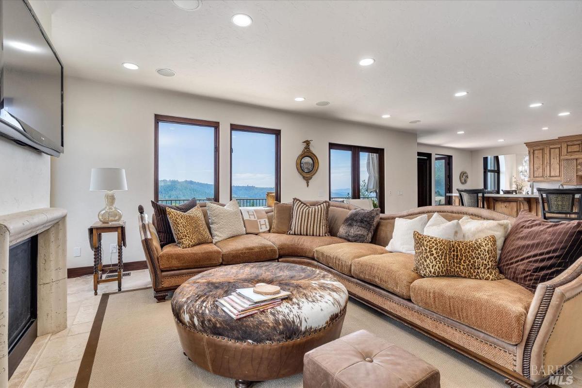 A family room with a sectional sofa, a round ottoman, and a fireplace.