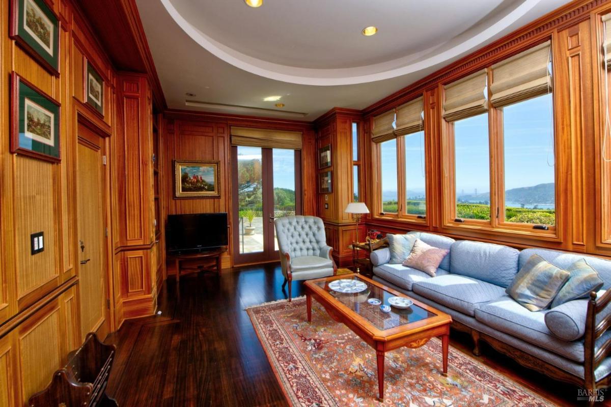 A spacious wood-paneled sitting room with large windows offering views of the landscape, a blue sofa, and a classic armchair.