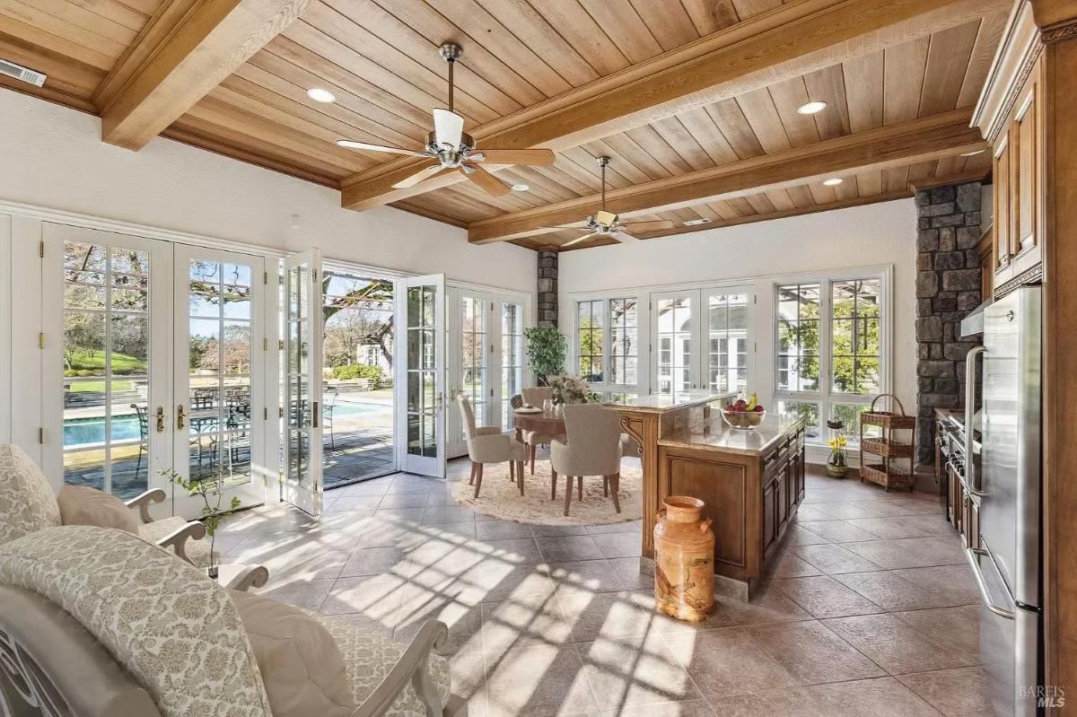 A sunroom with a wooden ceiling, fans, and an open view leading to an outdoor pool area.