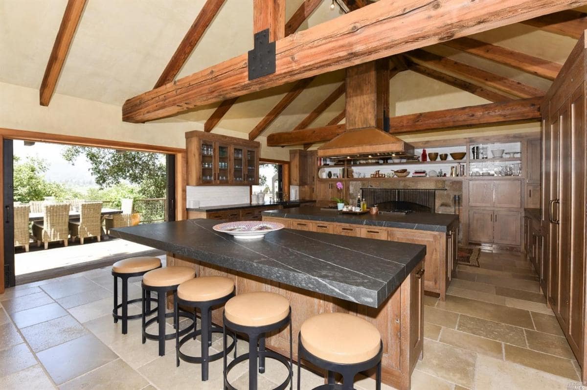 A kitchen with exposed wooden beams, a large island, and open shelving.