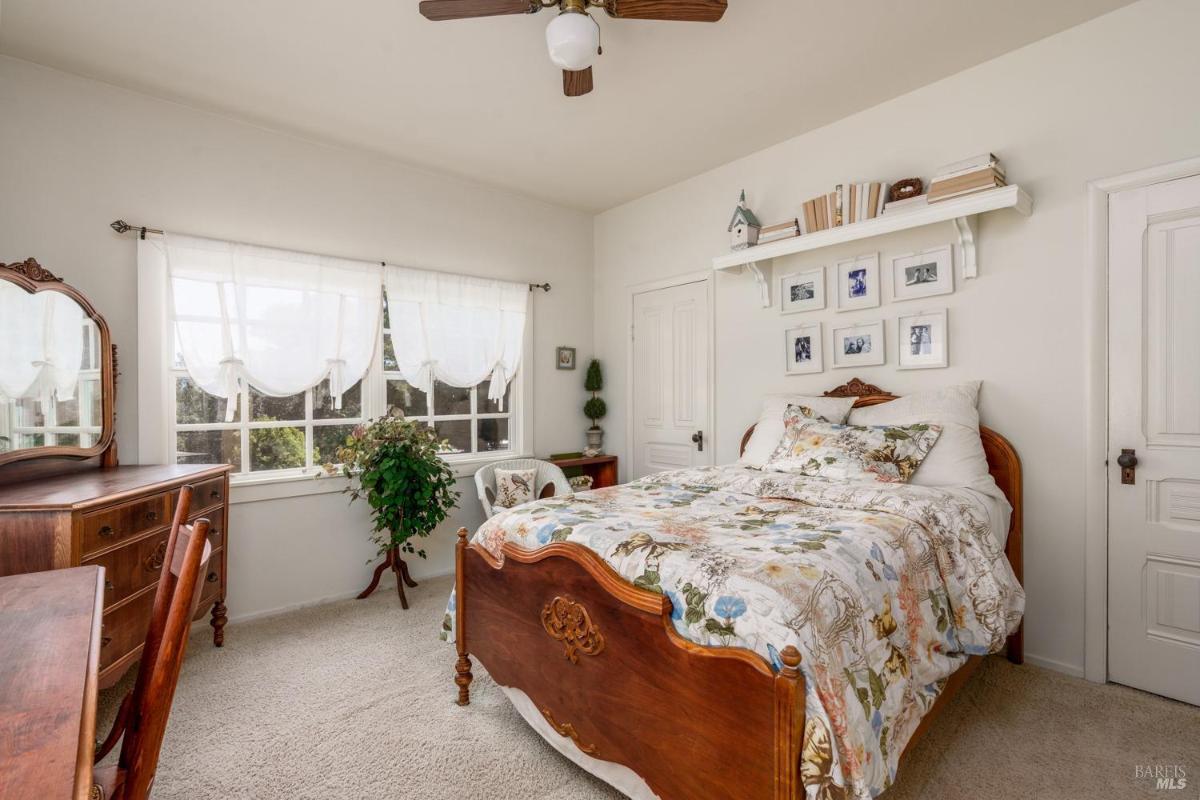 Bedroom with a floral bedspread, dresser, and large windows.