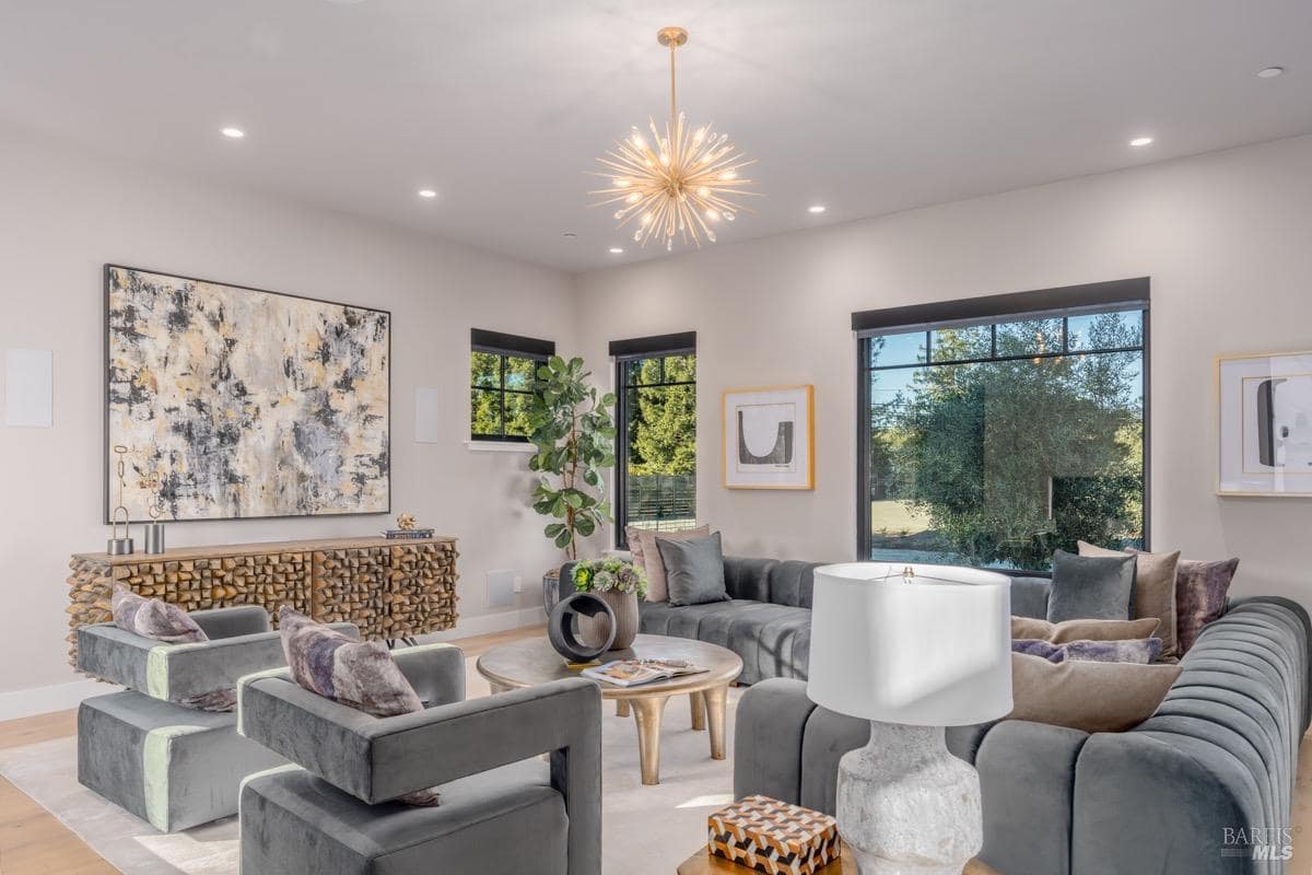 Living room with dark velvet sofas, accent chairs, large artwork, and a modern starburst chandelier.