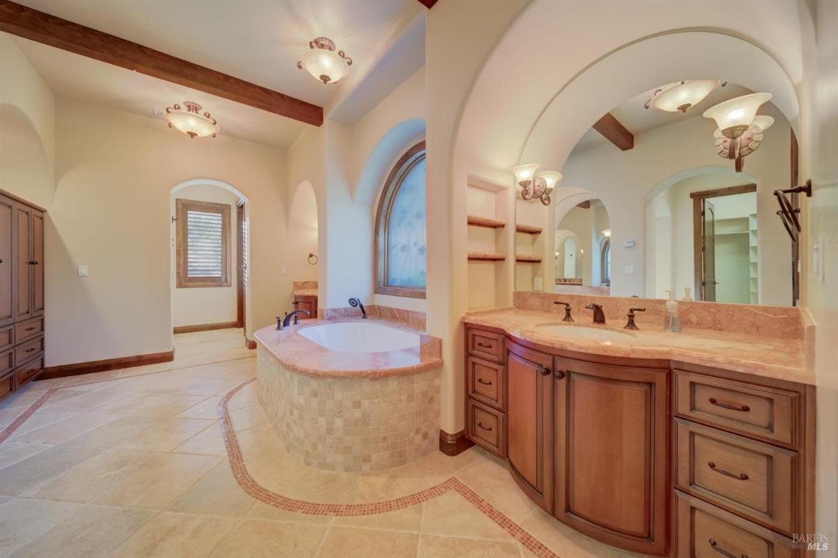 A spacious bathroom featuring a bathtub, dual sinks, and shelves.