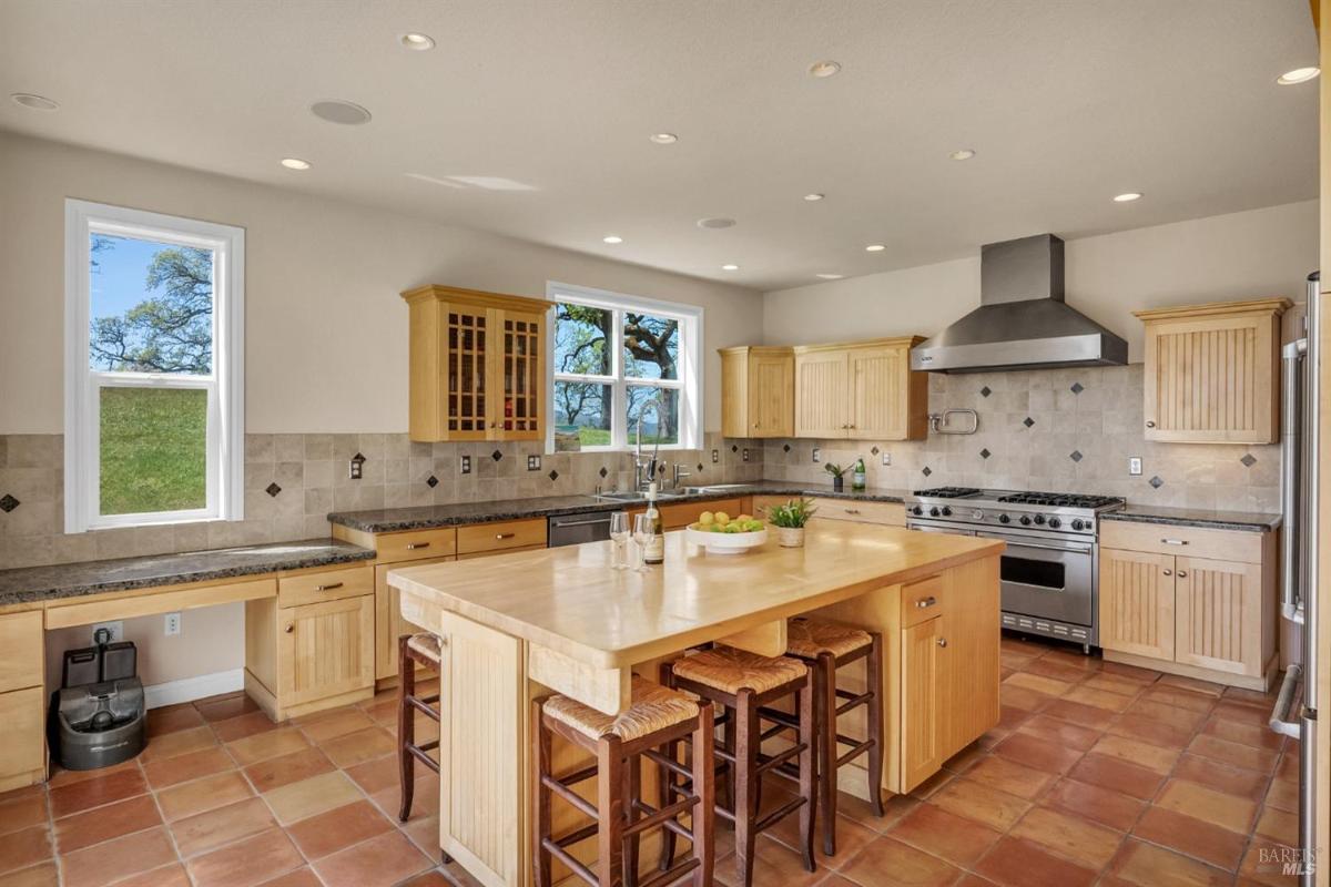 A kitchen with wooden cabinetry, a large island with bar stools, and stainless steel appliances.