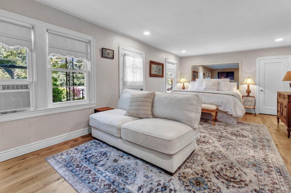 A bedroom with a sitting area, large windows, and a bed positioned against a mirrored wall.