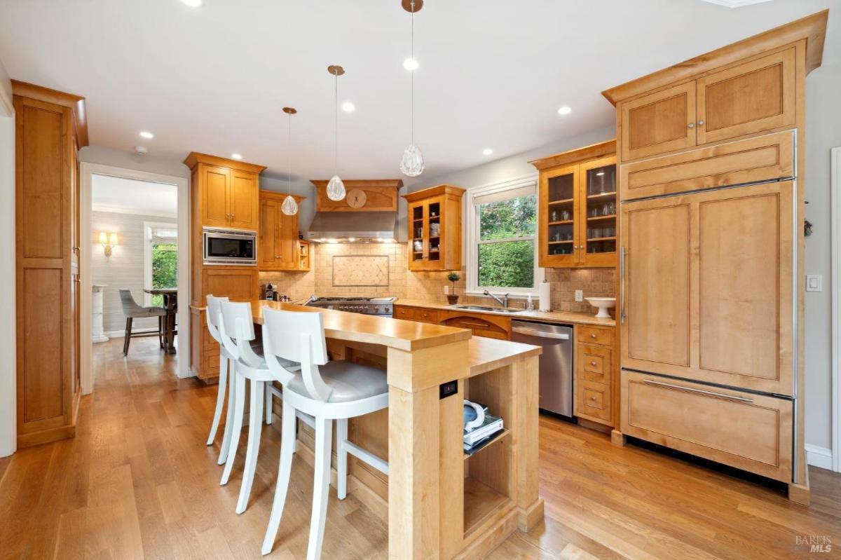 A kitchen with wooden cabinetry, a built-in refrigerator, and a breakfast bar with white stools.