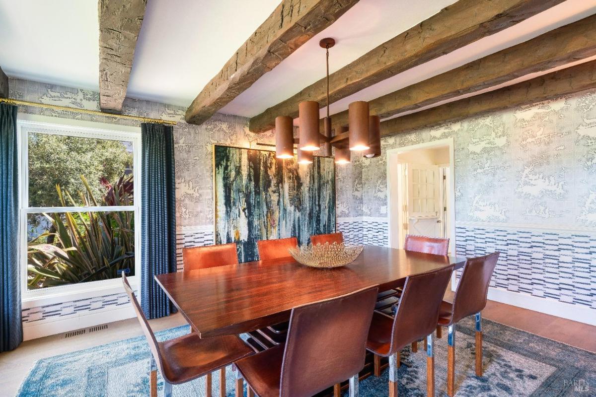 Dining room with wooden table, chairs, exposed beams, and wall artwork.