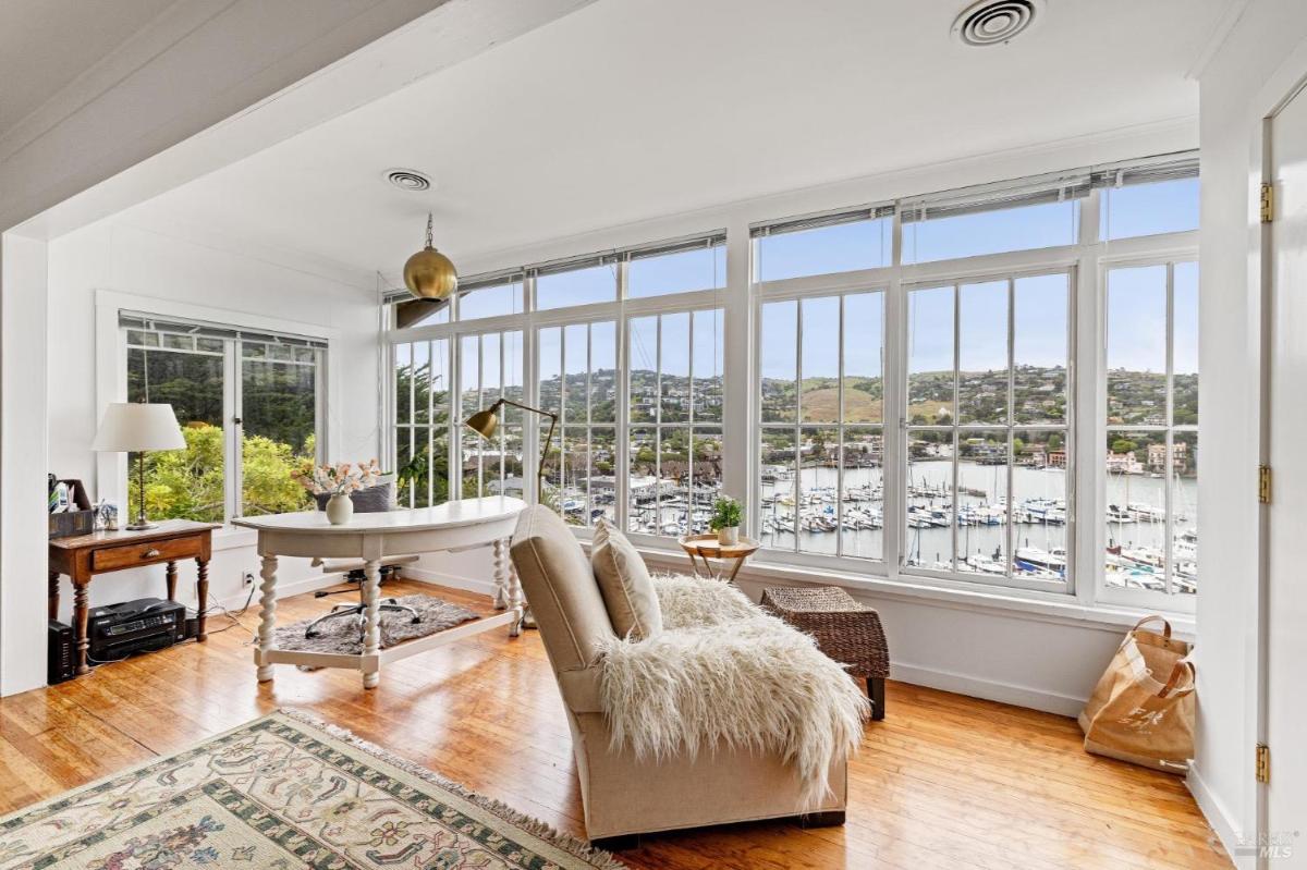 Home office with large windows and view of a marina and surrounding hills.