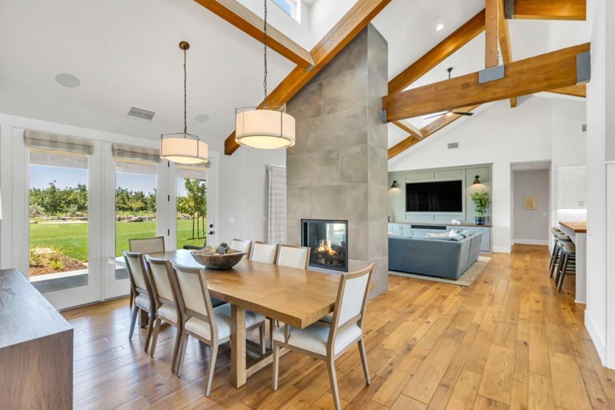 A dining room with a table, chairs, and large windows opening to an outdoor view.