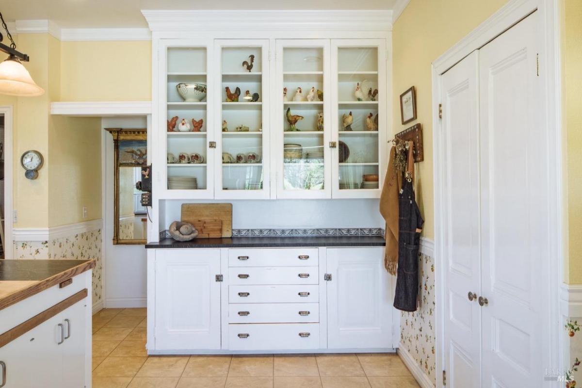 Kitchen storage area with white cabinetry and glass display shelves.