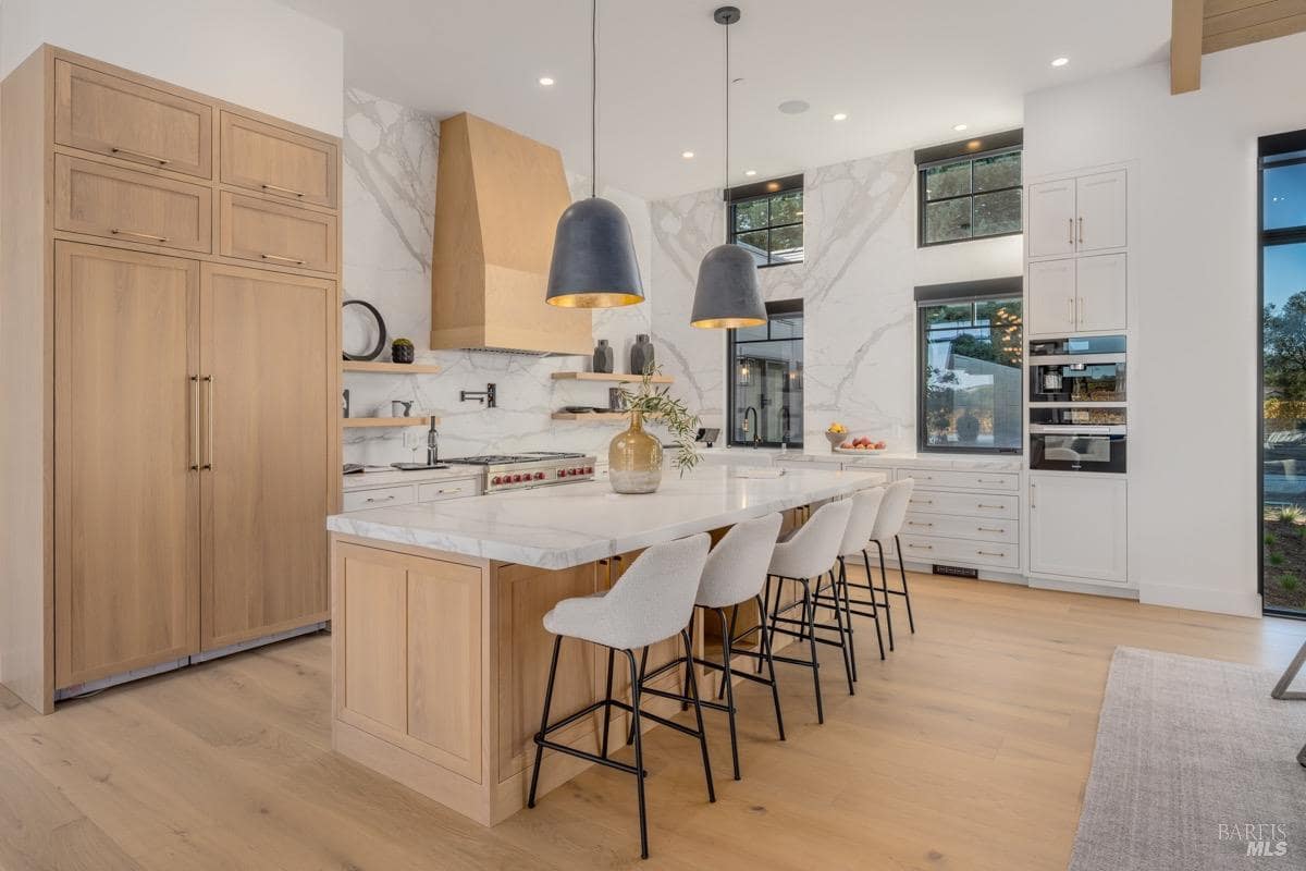 Modern kitchen with marble backsplash, large island seating, wood cabinetry, and pendant lighting.