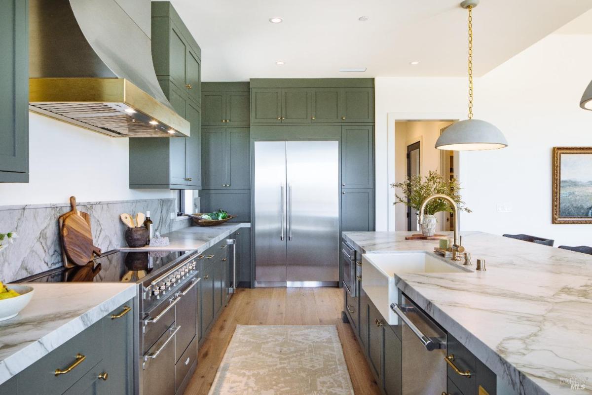 A modern kitchen with green cabinets, marble countertops, and stainless steel appliances.