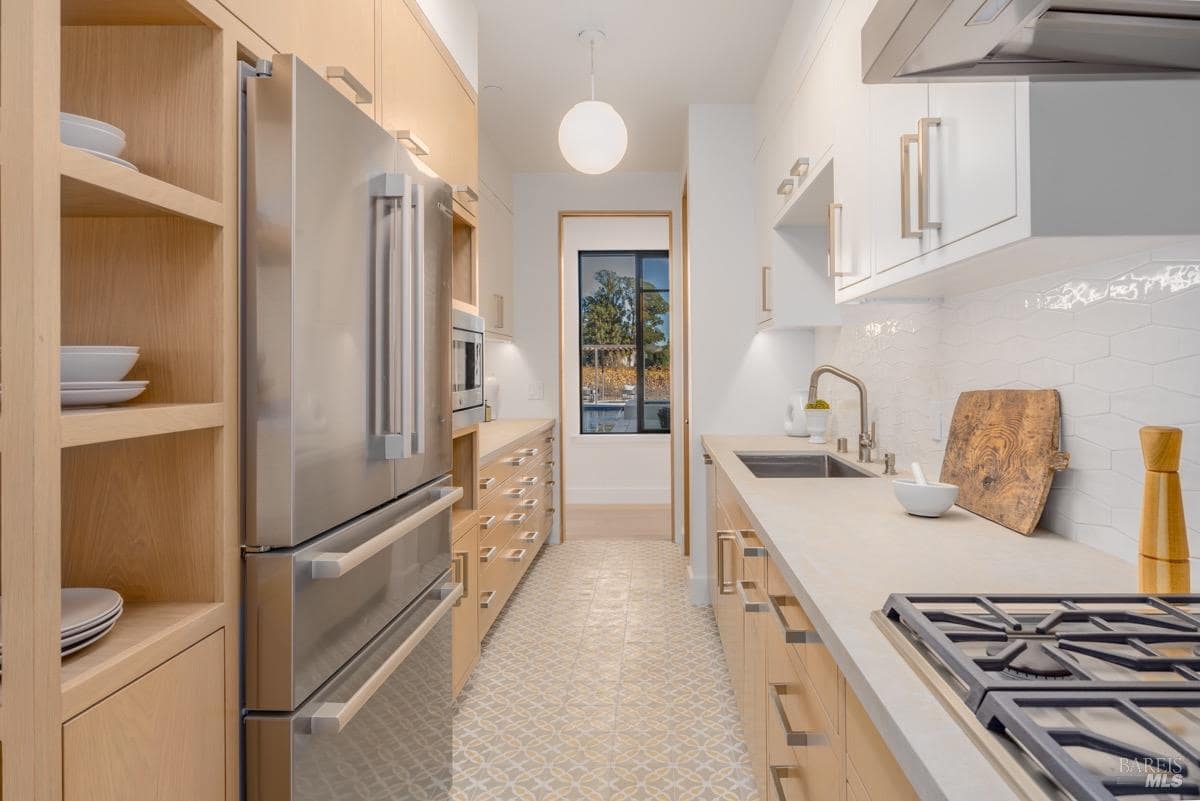 Galley kitchen with wood cabinetry, stainless steel appliances, white countertops, and hexagonal tile backsplash.