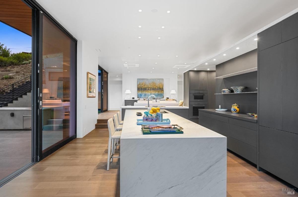 A modern kitchen with a large marble island, bar stools, and a dark cabinetry.