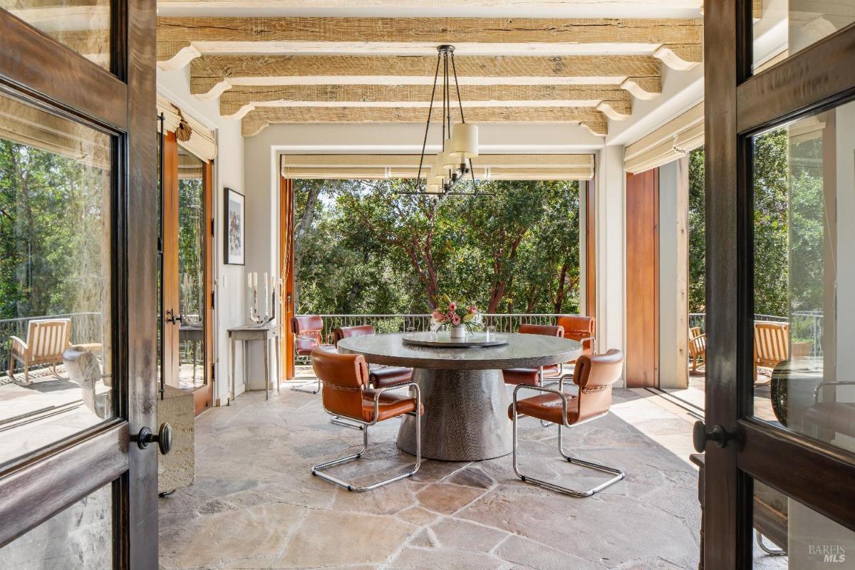 Breakfast nook with a round table, leather chairs, and views through large open doors.