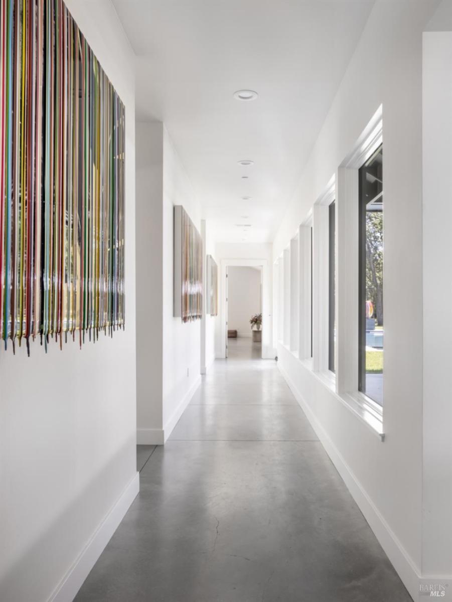 A hallway with polished concrete floors, large windows on one side, and colorful decor on the opposite wall.