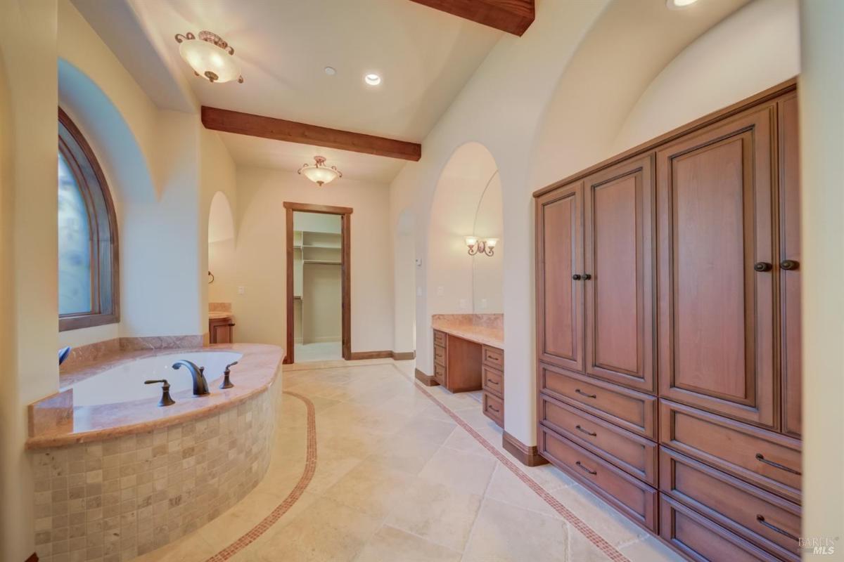 A bathroom with a bathtub, cabinetry, and arched windows.