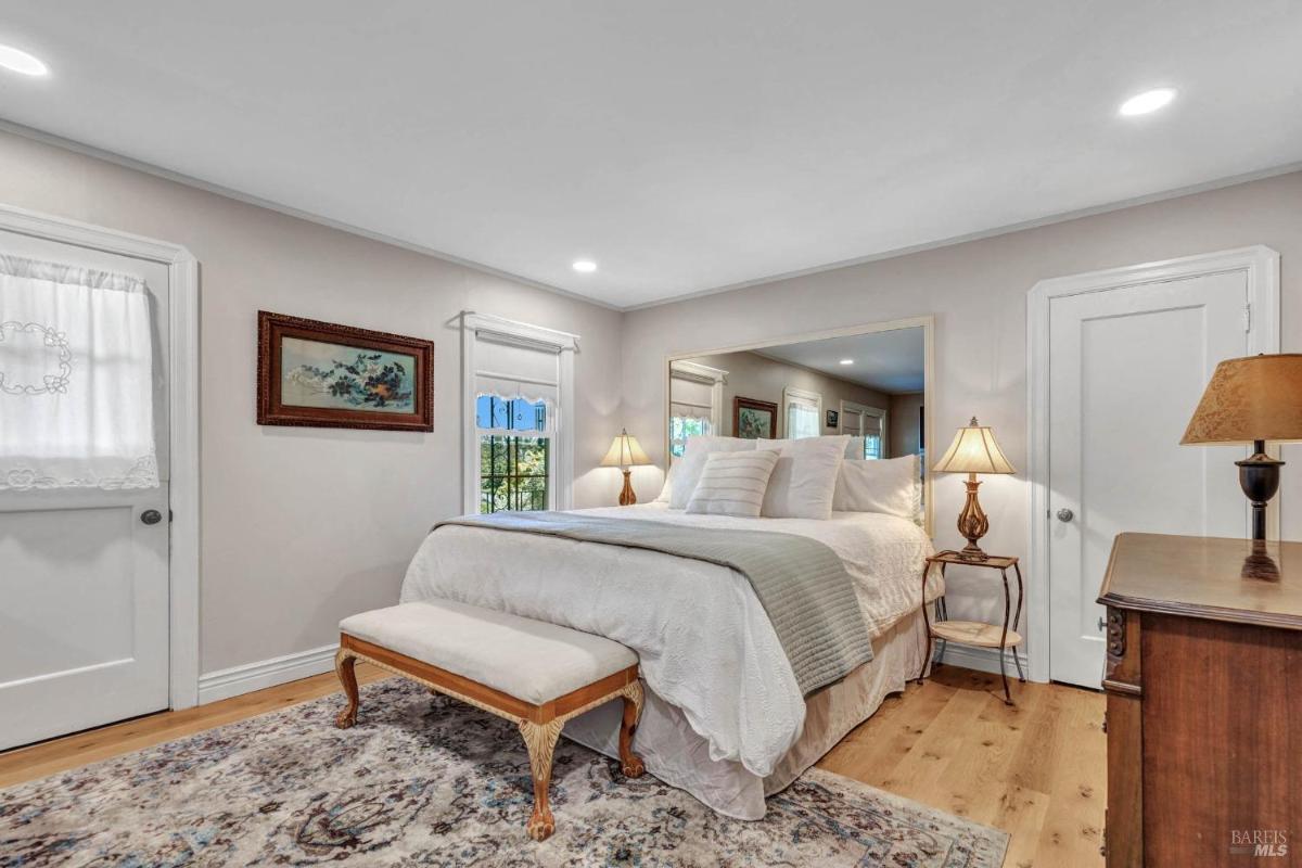 A bedroom with a sitting area, large windows, and a bed positioned against a mirrored wall.