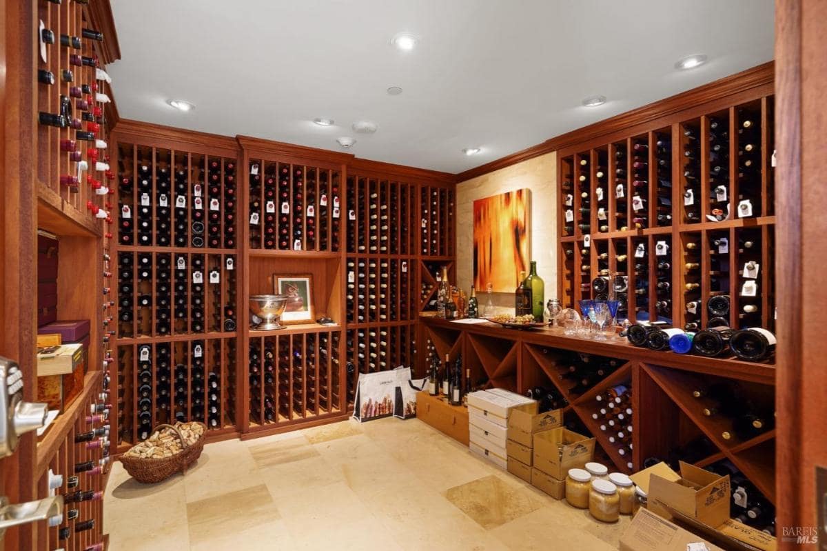 Wine cellar with wooden racks holding various wine bottles and storage boxes on the floor.