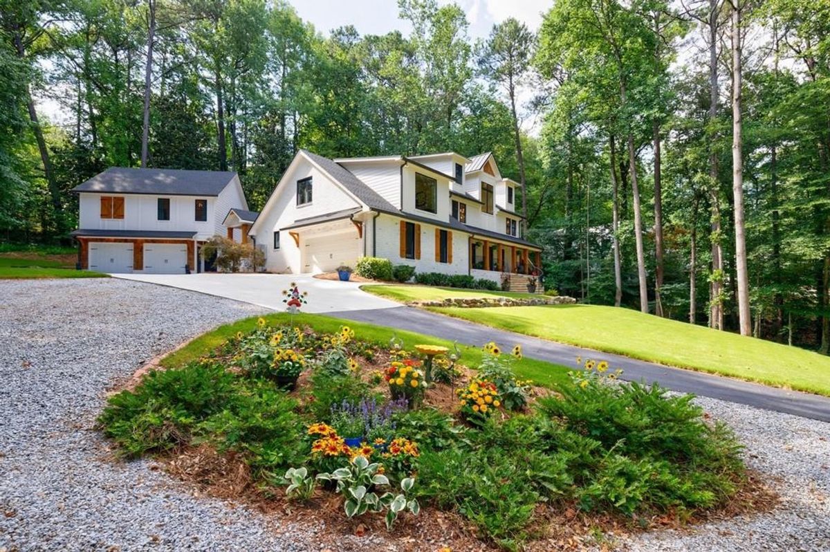 A picturesque property with a detached garage, vibrant landscaping, and a winding driveway framed by tall, mature trees.