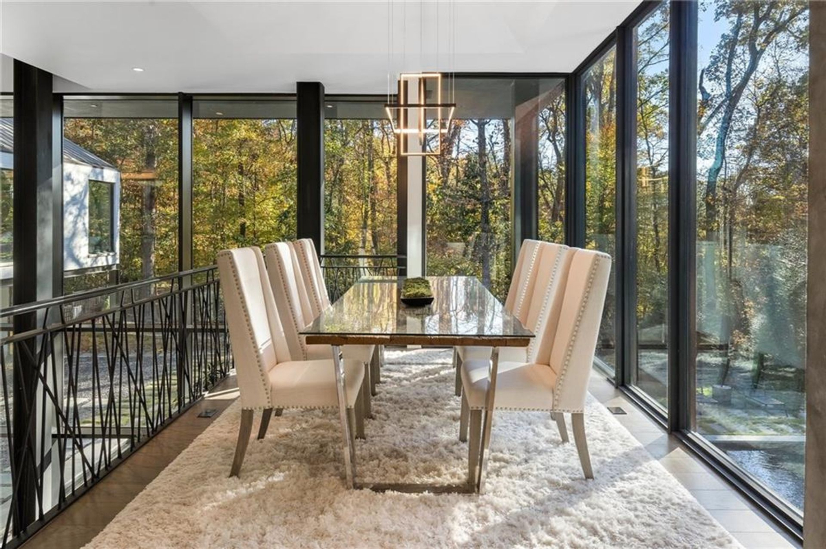 A sleek dining space with a polished stone table and plush chairs is bathed in natural light from floor-to-ceiling.