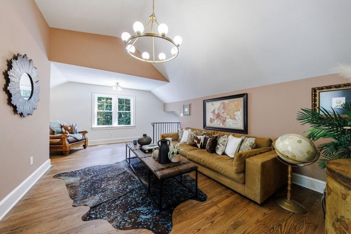 A cozy sitting area boasts a plush sofa, rustic decor, and a unique cowhide rug, illuminated by a stylish chandelier.