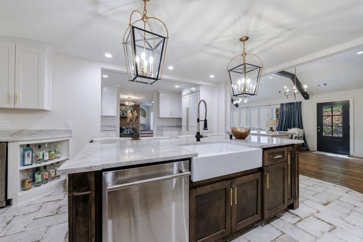 A modern farmhouse kitchen showcases marble countertops, a deep farmhouse sink, rustic wooden cabinetry, and elegant lantern-style pendant lighting.