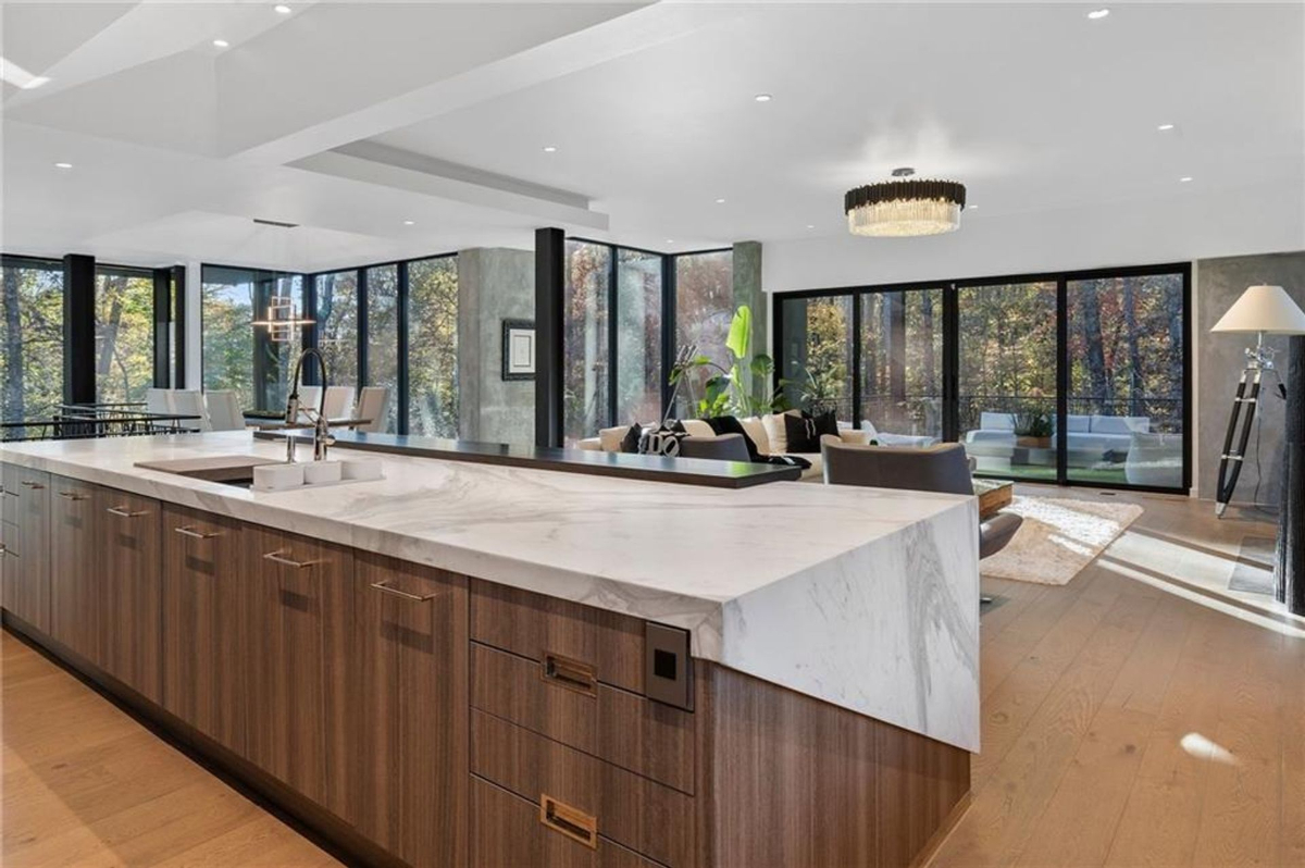 Kitchen island flows into a bright, open living area framed by floor-to-ceiling glass doors.