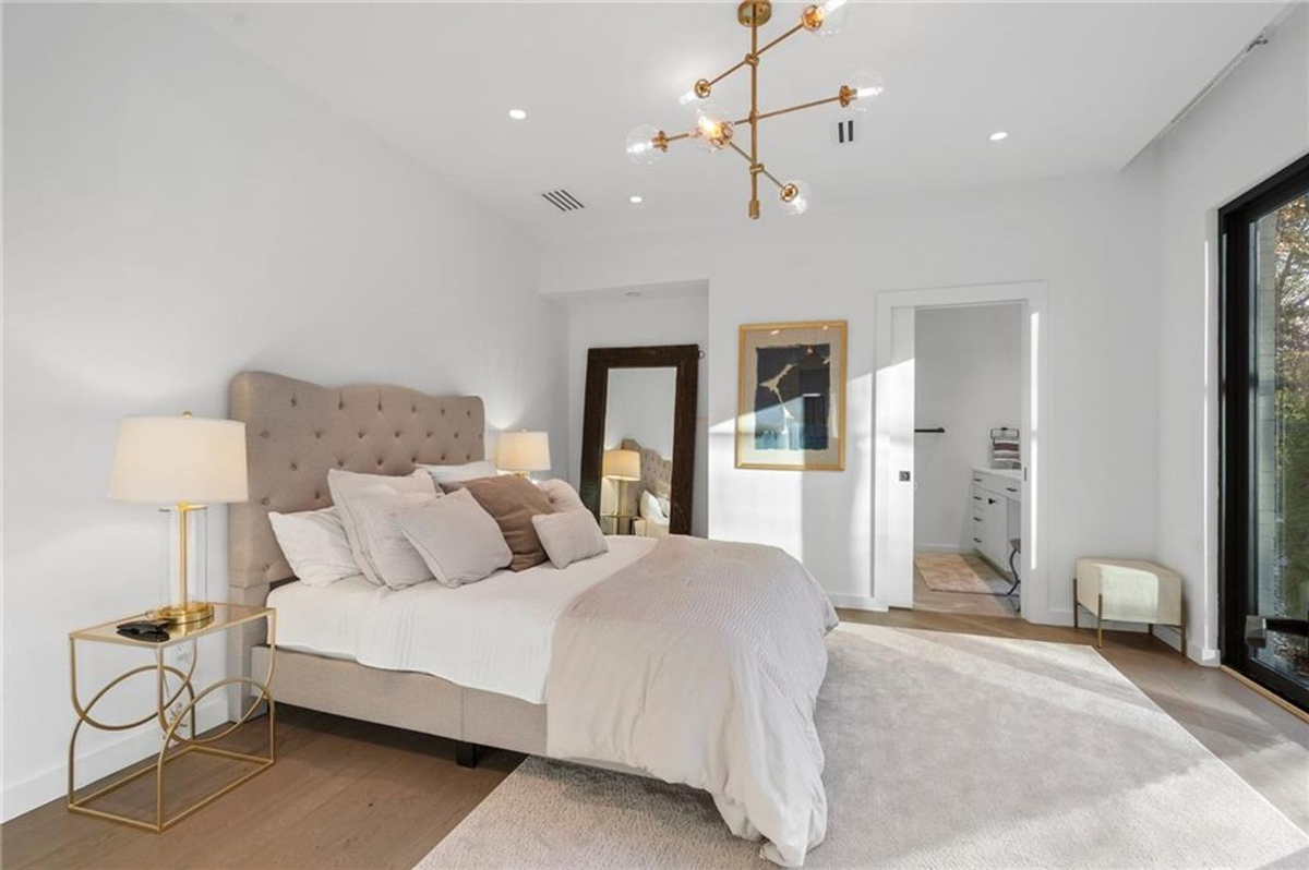 A chic bedroom showcases a tufted bed, modern gold accents, and an airy layout that flows seamlessly into an elegant en-suite bathroom.