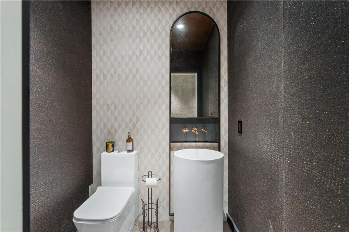 A chic powder room features textured walls, a modern pedestal sink, and elegant gold fixtures for a luxurious touch.