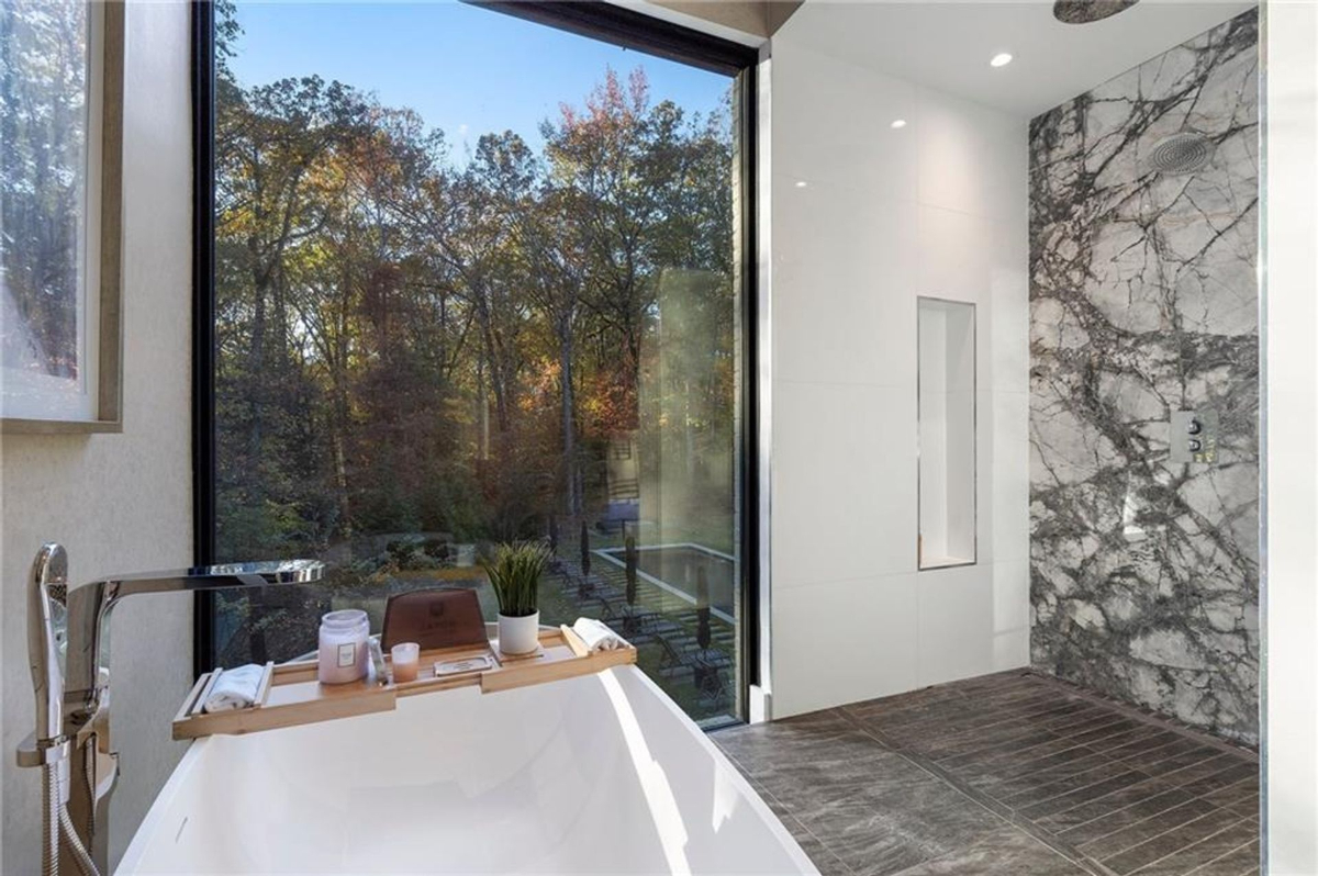 A serene bathroom offers a freestanding tub with wooded views and a spacious marble-accented walk-in shower.