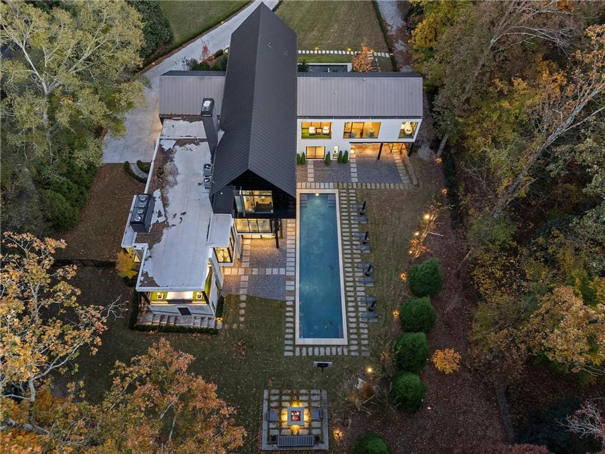 An aerial view highlights a modern architectural masterpiece, featuring a sleek pool, landscaped grounds, and a wooded backdrop creating a private retreat.