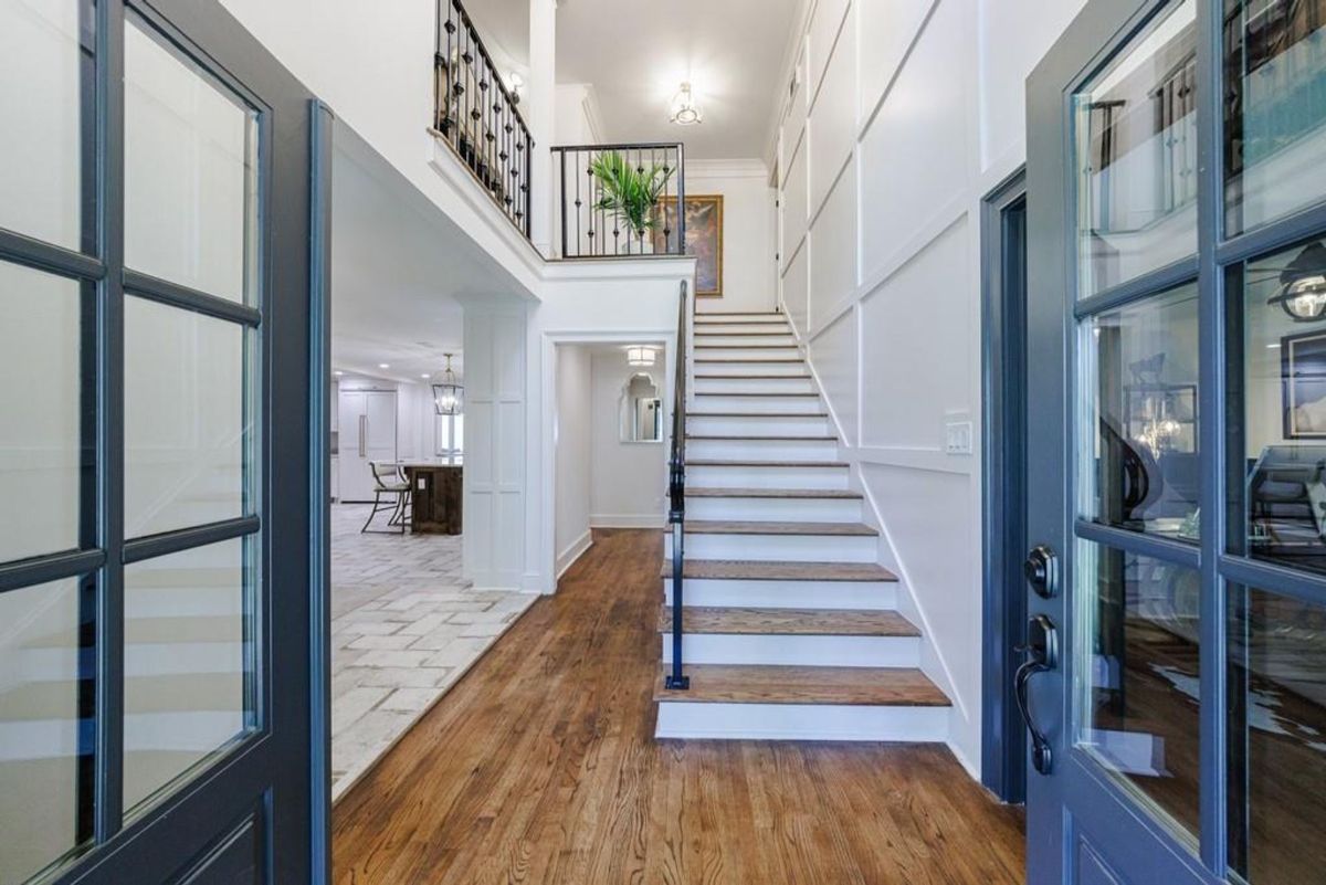 Open and elegant entryway features rich hardwood floors, white panel walls, and an iron-railed staircase leading to a second-floor landing.