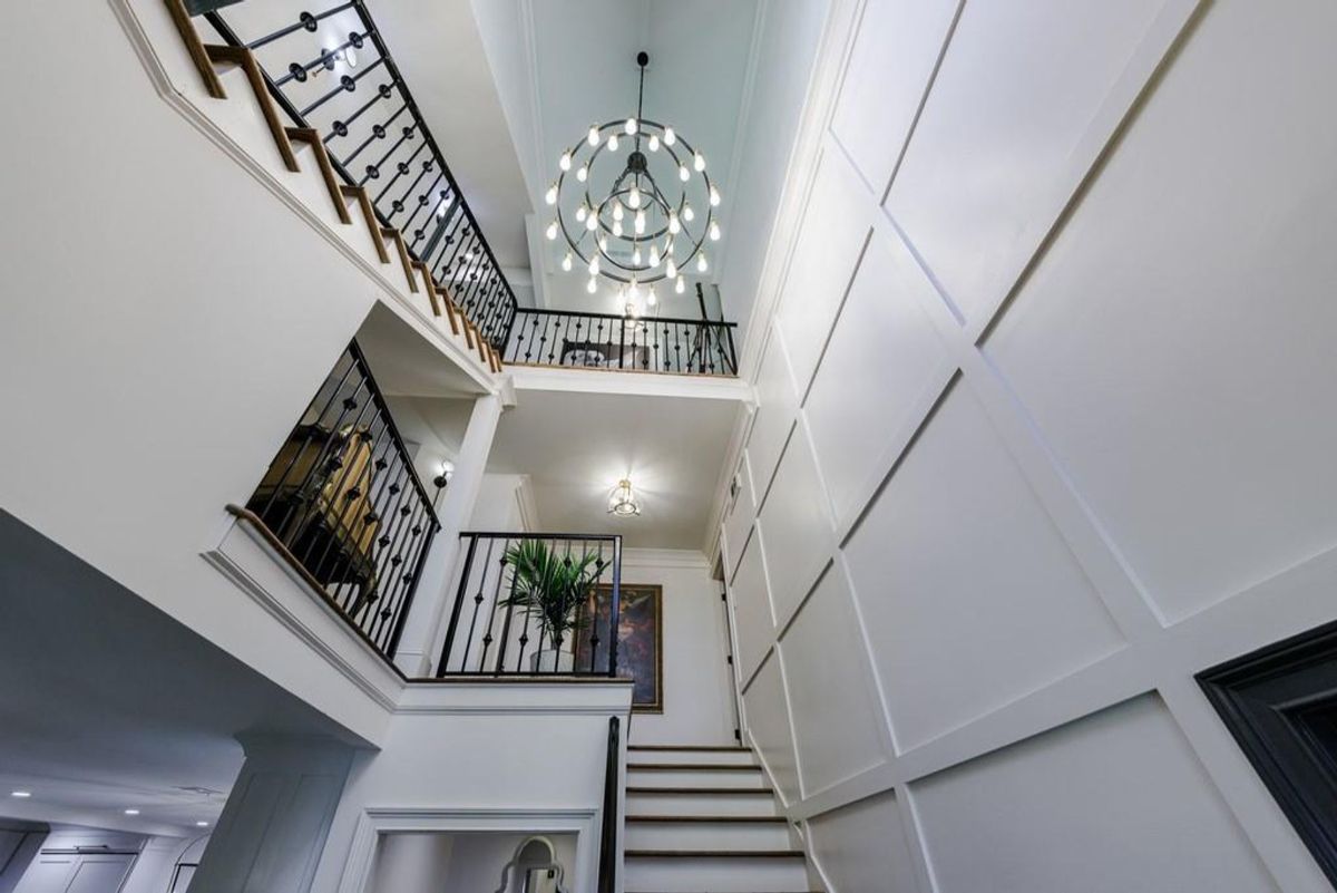 Stunning two-story foyer features a modern chandelier, iron railings, and elegant wall paneling.