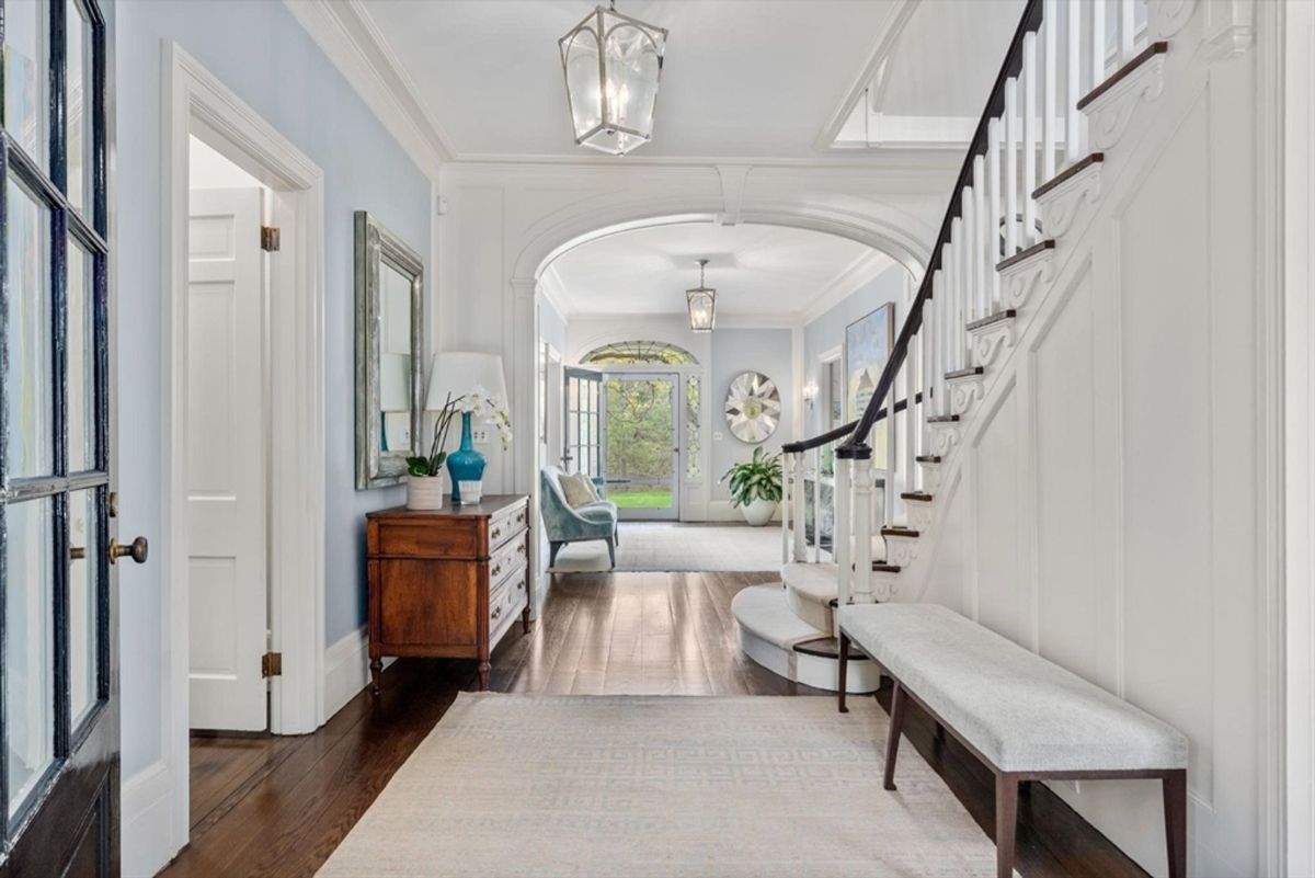 A beautifully lit hallway features rich hardwood flooring, intricate molding, and a seamless transition to the bright sitting area and entryway.