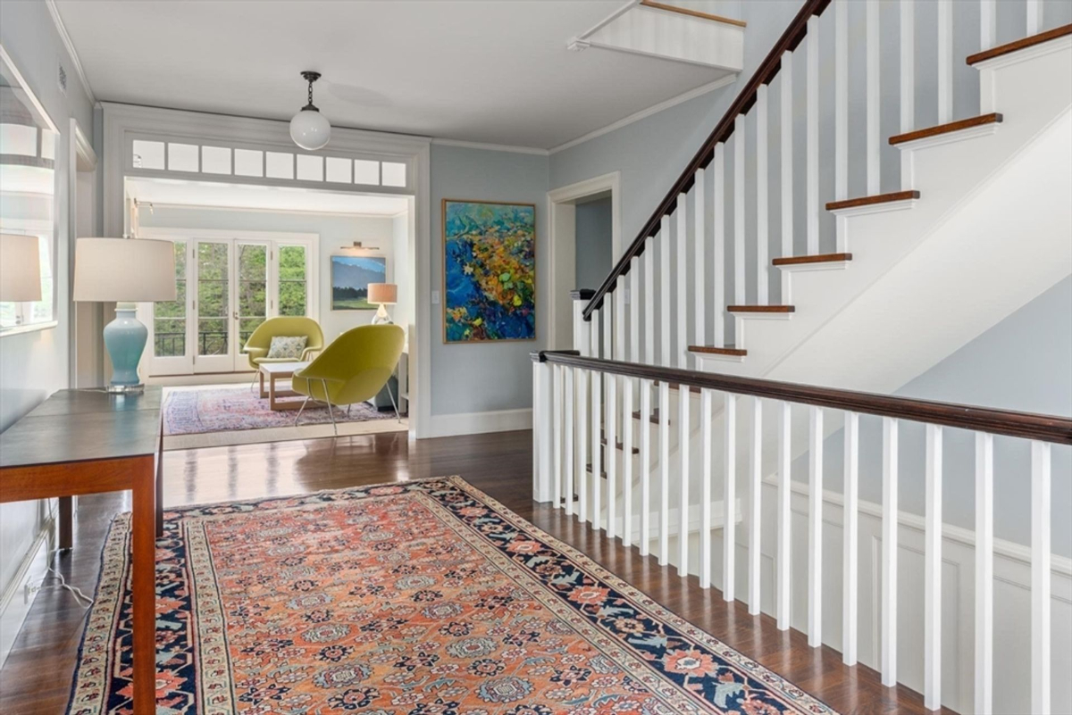 A vibrant hallway connects to a cozy sitting area with large windows and modern lime green chairs, enhanced by colorful artwork and natural light.