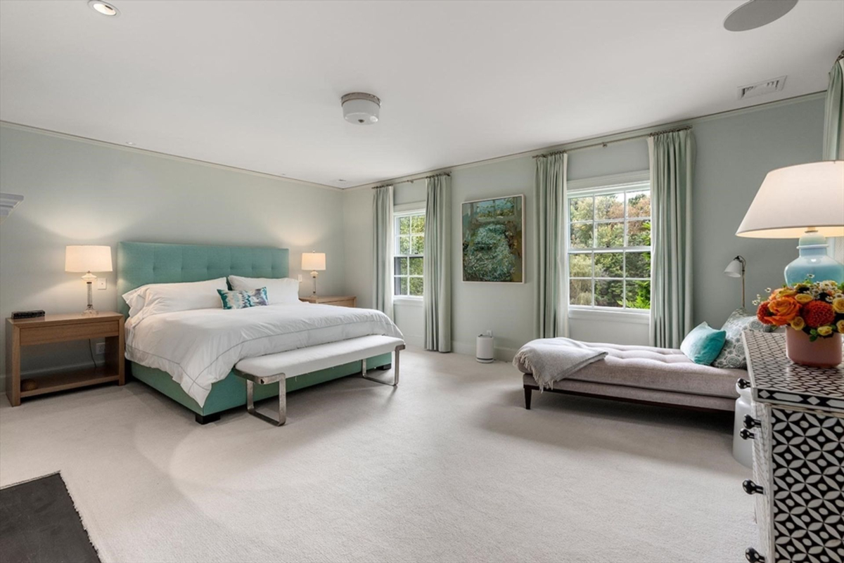 Bedroom features soft pastel tones, a tufted headboard, and large windows overlooking lush greenery.