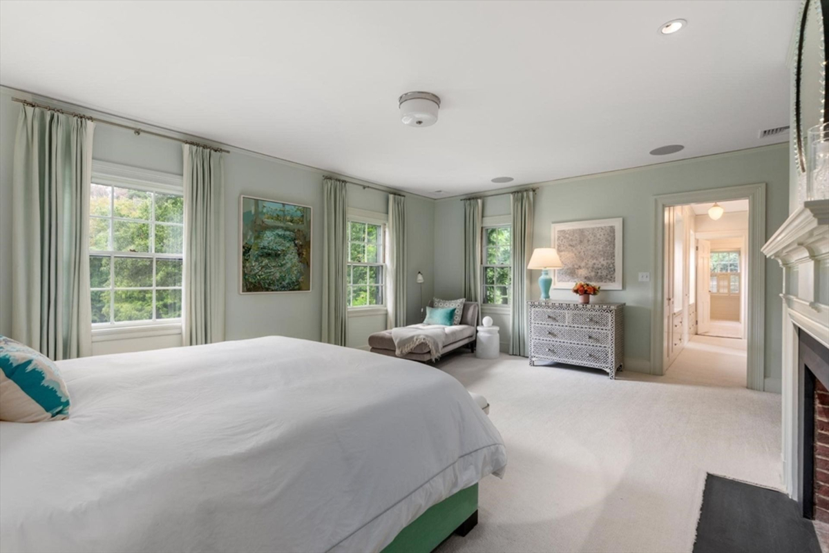 A bright and airy bedroom features soft green walls, multiple large windows, and a cozy chaise lounge for relaxing.