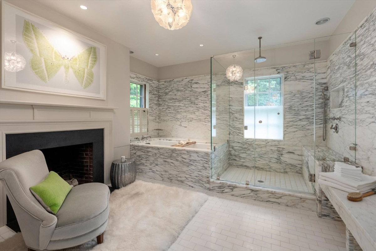 An opulent bathroom showcases floor-to-ceiling marble, a glass-enclosed shower, a soaking tub, and a cozy sitting area by the fireplace.