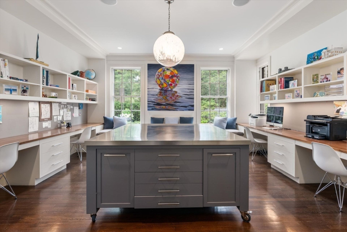 A modern workspace features a large central island, built-in desks, and shelves under bright natural light for an inspiring environment.