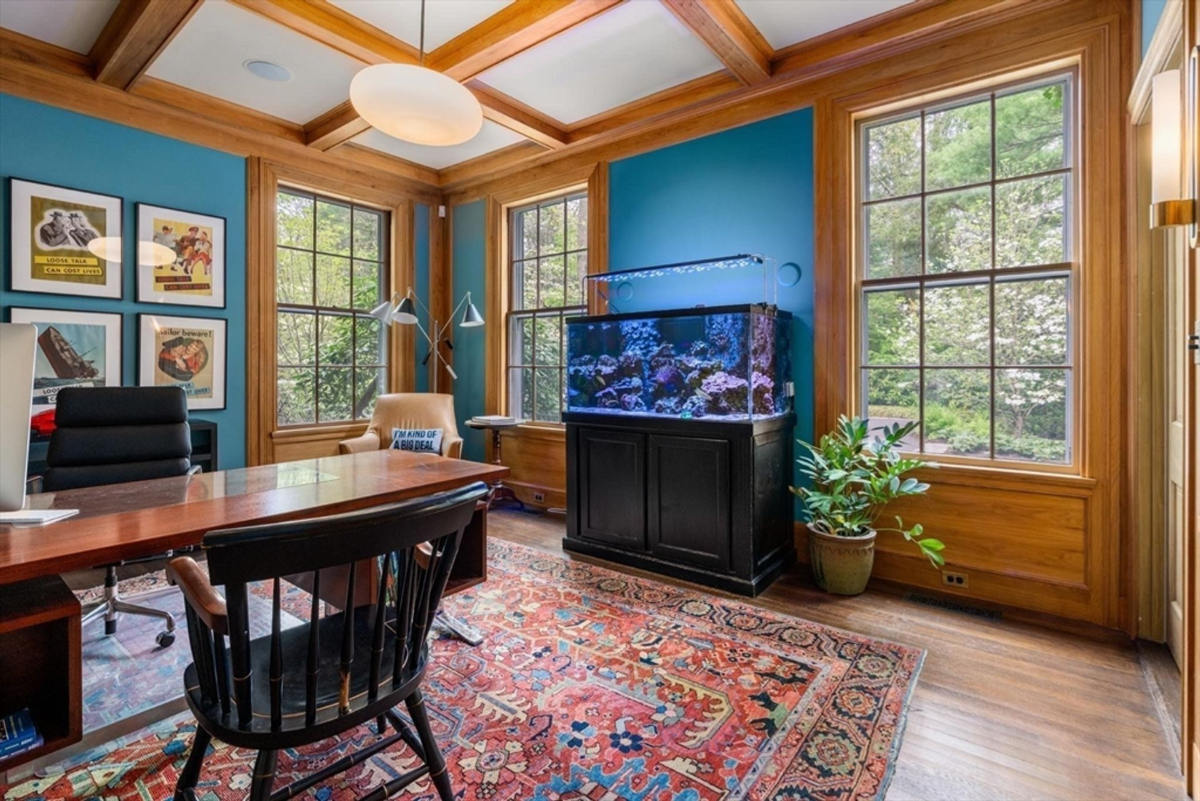 A vibrant office space showcases coffered wood ceilings, a colorful area rug, and an illuminated aquarium accentuating its unique charm.