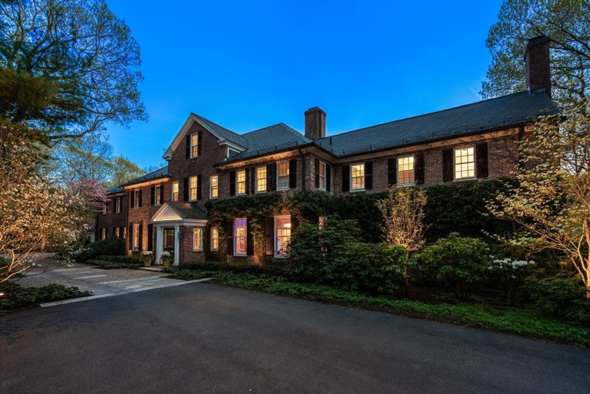 Brick Colonial radiates charm as its evening glow illuminates the surrounding lush greenery.