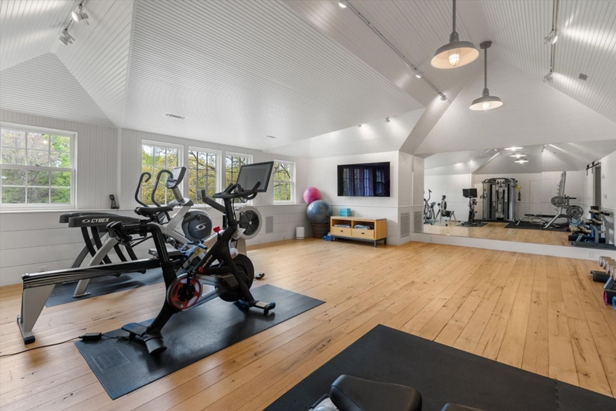 Home gym features vaulted beadboard ceilings, natural wood flooring, and mirrored walls for a versatile workout experience.