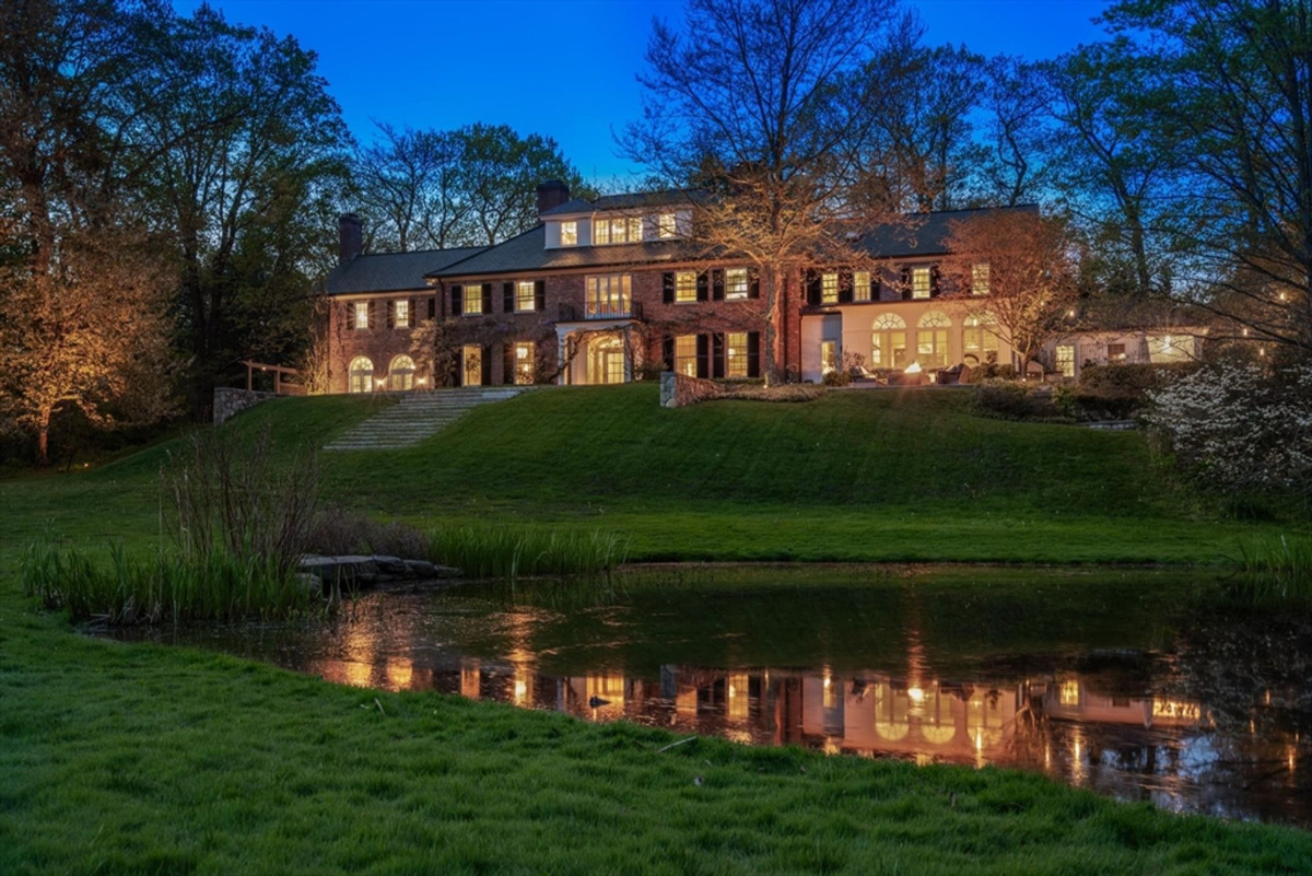 The illuminated estate casts a stunning reflection over the serene pond, creating a picturesque evening scene.