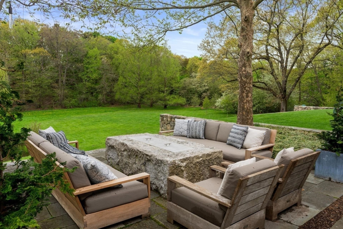 Outdoor seating is paired with a rustic stone fire table, surrounded by serene greenery.