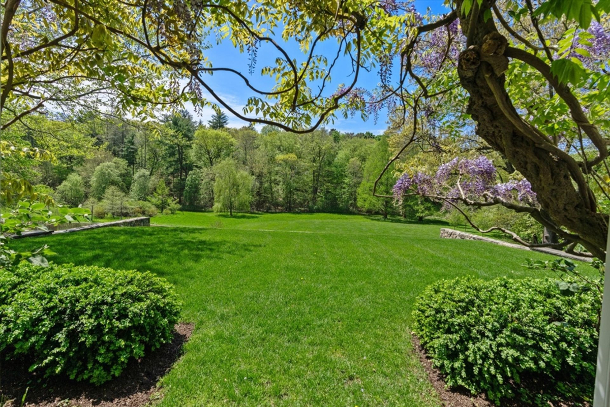 Vibrant green lawns stretch out under a clear sky, framed by flowering wisteria and lush foliage.