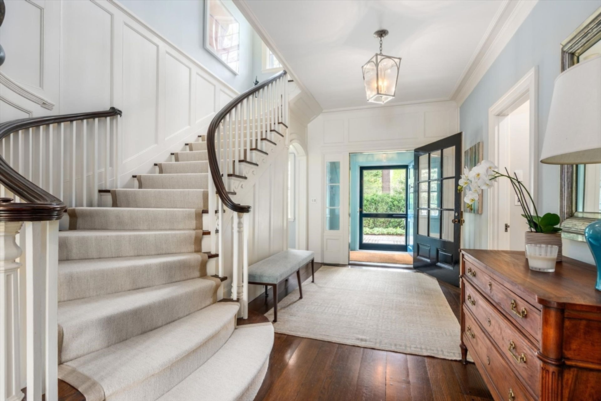 An inviting foyer showcases a gracefully curved staircase and sunlit accents, setting a warm and elegant tone.