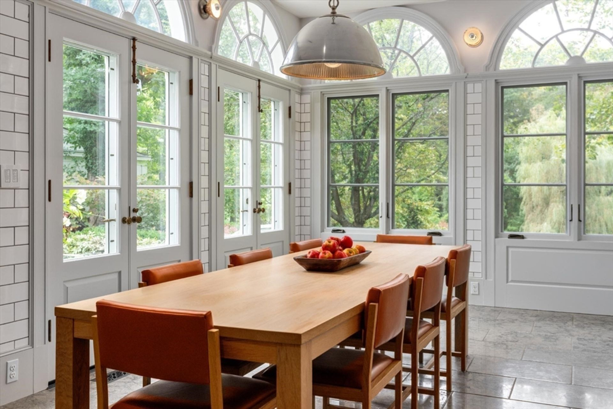 An elegant dining space bathed in natural light from large arched windows offers serene views of the lush outdoors.