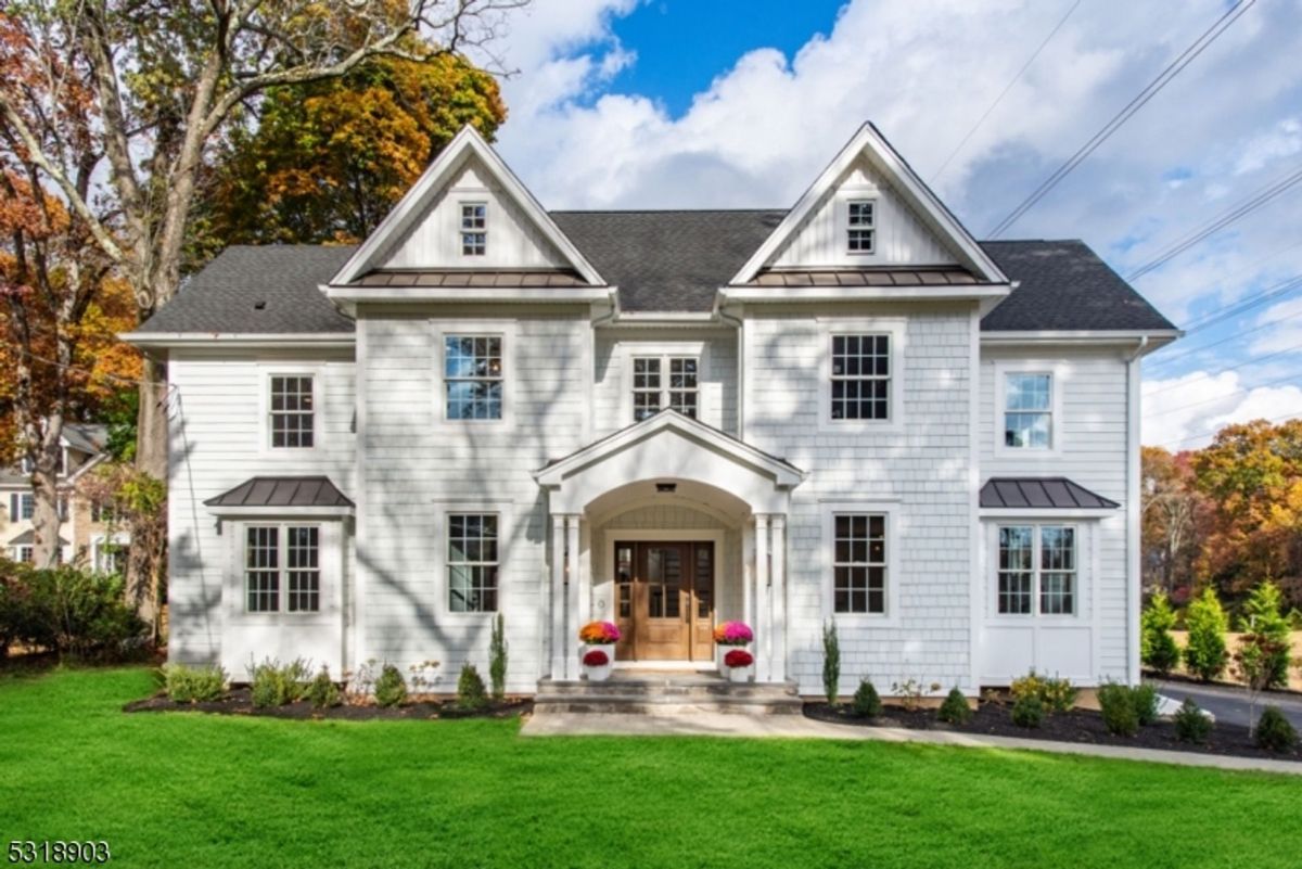 Elegant colonial-style home boasts crisp white siding, a welcoming covered entryway, and a lush green lawn surrounded by mature trees.