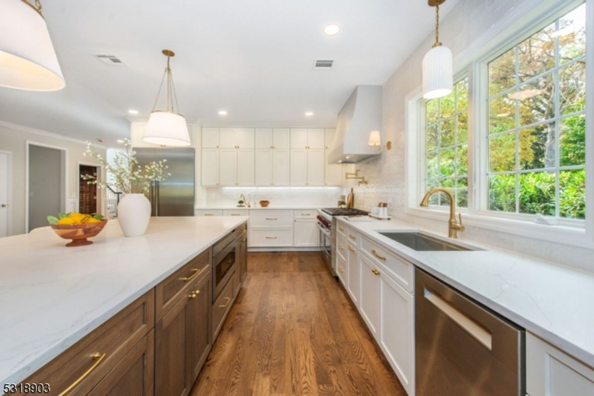 Bright kitchen features custom cabinetry, elegant gold hardware, and expansive countertops with large windows offering garden views.